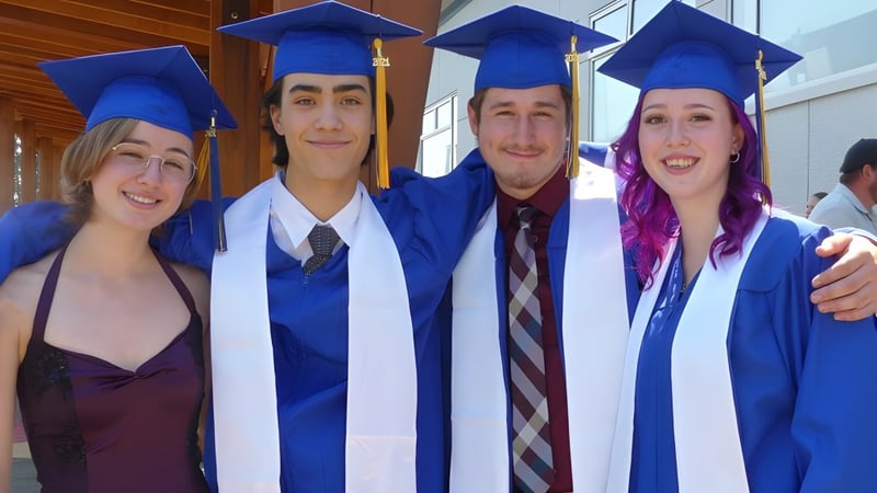 Vier Absolventen der Ballenas Secondary School posieren gemeinsam in ihren Abschlusskleidern in einer schulischen Umgebung.