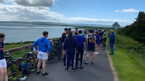 Eine Gruppe von Schülerinnen und Schülern der Ballingarry Presentation School steht auf einem Pfad mit Blick auf einen See und bewaldete Hügel.