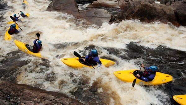 Schüler der Ballingarry Presentation School beim Wildwasser-Rafting durch einen schäumenden Fluss in felsiger Umgebung.