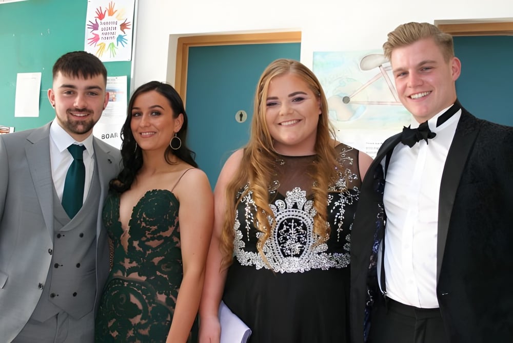 Vier Personen in formeller Kleidung posieren gemeinsam bei einer Veranstaltung der Ballinteer Community School.