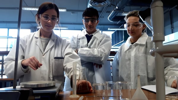 Drei Personen in weißen Laborkitteln stehen im Labor der Ballinteer Community School um wissenschaftliche Geräte.