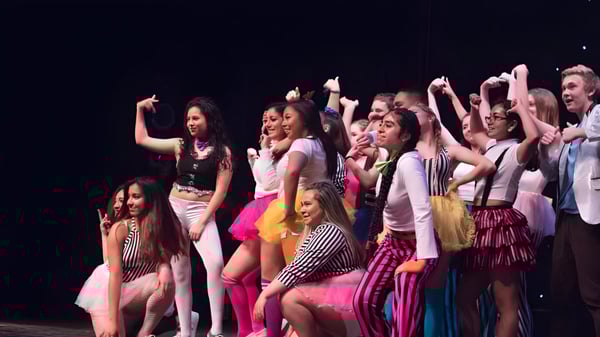 Eine Gruppe junger Schülerinnen des Ballybay Community College führt einen Auftritt auf der Bühne vor dunklem Hintergrund vor.