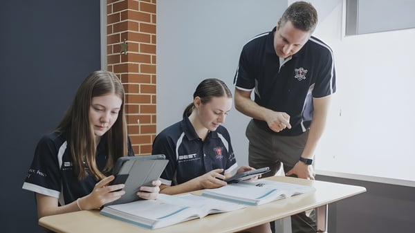 Drei Schüler nutzen elektronische Geräte an einem Tisch auf dem Campus des Ballybay Community College.