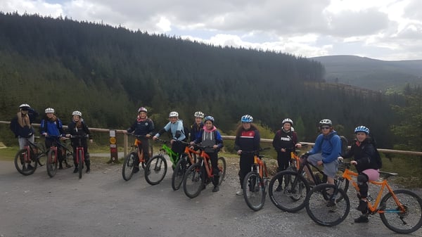 Eine Gruppe Fahrrad fahrender Schüler steht auf einem Waldweg auf dem Gelände des Banagher College vor bewölktem Himmel.