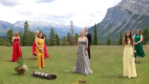 Eine Gruppe Schülerinnen steht in bunten Kleidern auf einer Wiese vor Bergen auf dem Gelände der Banff Community High School.