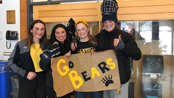Vier Schülerinnen stehen vor einem Gebäude der Banff Community High School und halten ein Schild mit der Aufschrift ‚Go Bears‘.