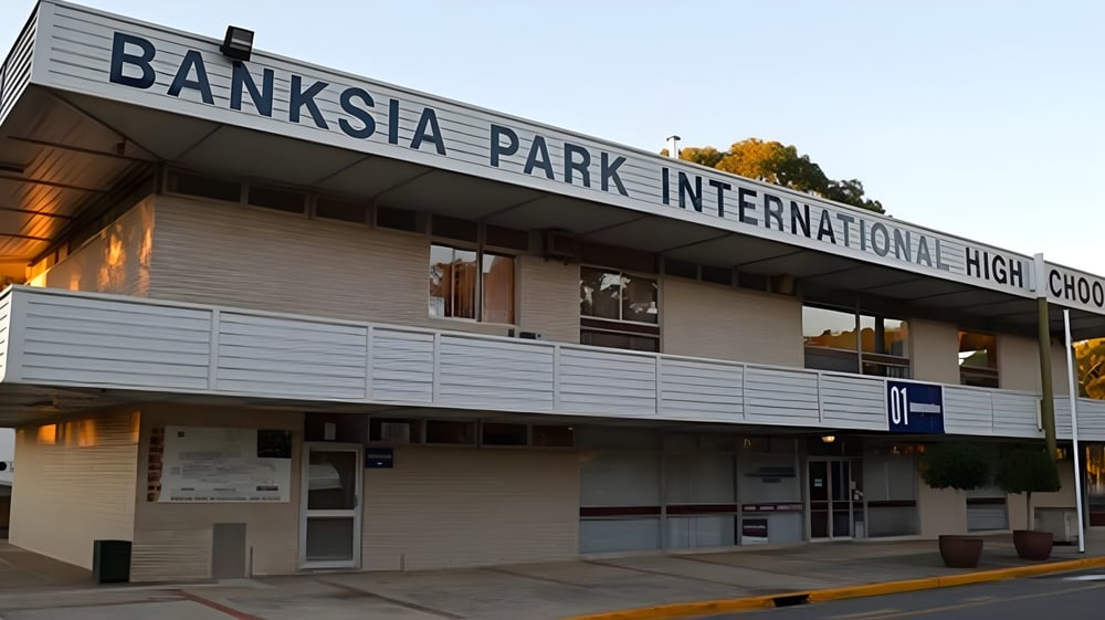 Der Eingangsbereich der Banksia Park International High School mit einem gut sichtbaren Schild vor Bäumen und blauem Himmel.