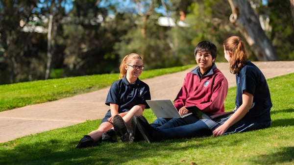 Drei Schüler der Banksia Park International High School sitzen auf einer Wiese mit Bäumen im Hintergrund.