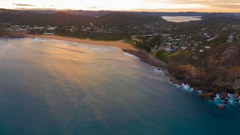 Luftaufnahme einer Küstenstadt mit grünen Hügeln und türkisfarbenem Meer in der Nähe von Barrenjoey High School.