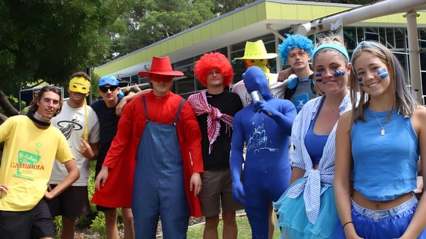 Eine Gruppe von Schülerinnen und Schülern der Barrenjoey High School trägt bunte Kostüme und steht draußen vor Bäumen und Gebäuden.