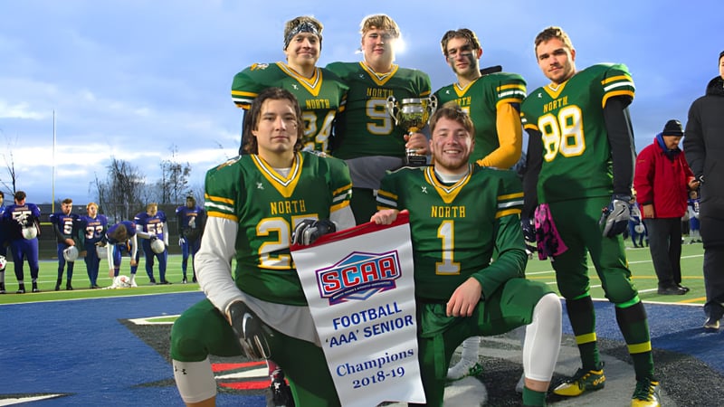 Fußballspieler des Barrie North Collegiate Institute halten ein Meisterschaftsbanner auf dem Spielfeld vor Zuschauern.