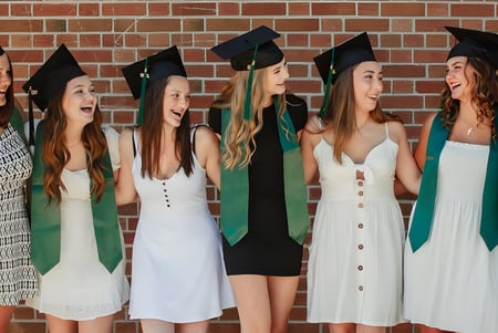Eine Gruppe Schülerinnen in Abschlusskleidung steht vor einer Backsteinwand auf dem Campus des Barrie North Collegiate Institute und feiert ihren Abschluss.