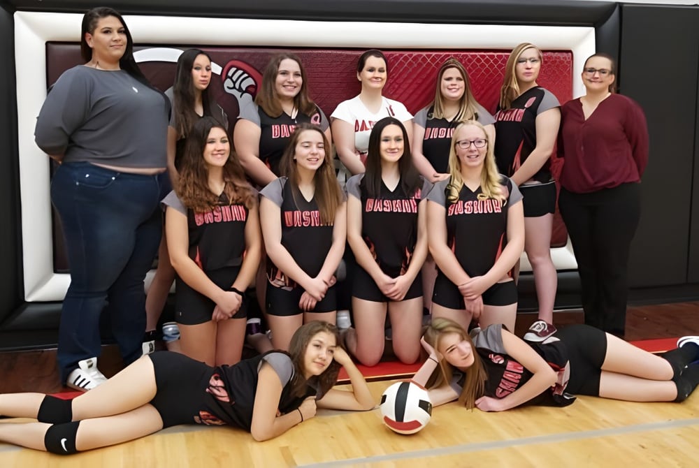 Eine Gruppe von Schülerinnen der Bashaw School posiert gemeinsam als Volleyballteam auf einem Holzspielplatz.