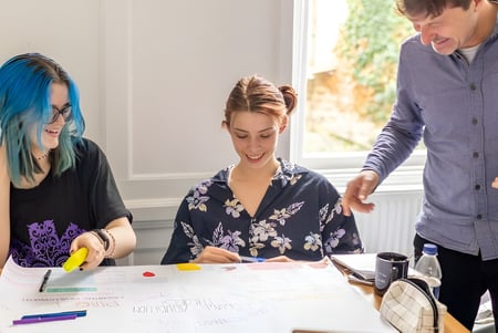 Schüler der Bath Academy arbeiten gemeinsam an einem Kunstprojekt mit verschiedenen Materialien am Tisch.
