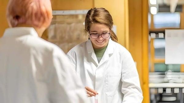Eine junge Frau im weißen Laborkittel steht lächelnd im Labor der Bath Academy.