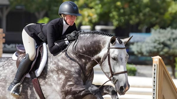 Eine Schülerin der Battle Abbey School reitet ein graues Pferd im Freien vor Bäumen und Gebäuden.