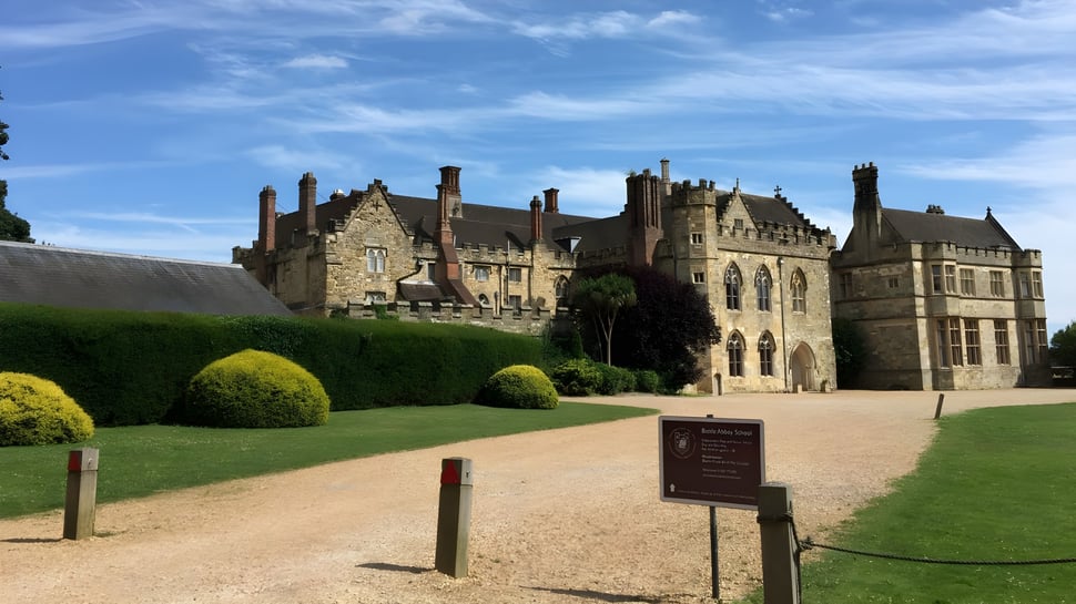 Das mittelalterliche Schloss auf dem Gelände der Battle Abbey School mit gepflegtem Rasen und Kiesweg im Vordergrund.