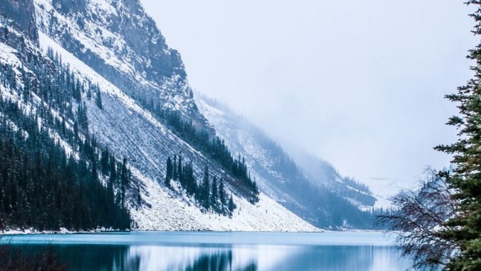 Ein schneebedecktes Bergpanorama mit einem türkisfarbenen See und immergrünen Bäumen vor dem Campus der Bawlf School.