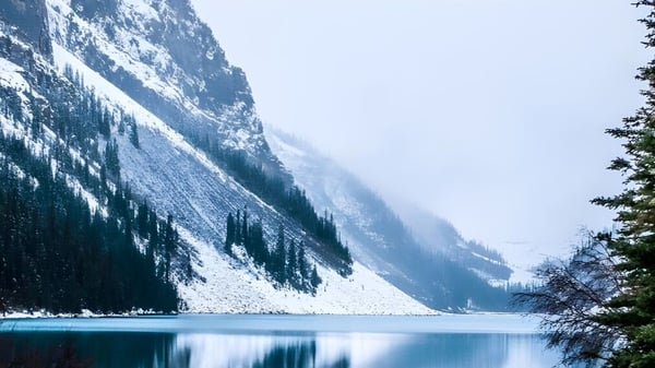 Ein ruhiger See mit türkisfarbenem Wasser und schneebedeckten Bergen im Hintergrund bei der Bawlf School.