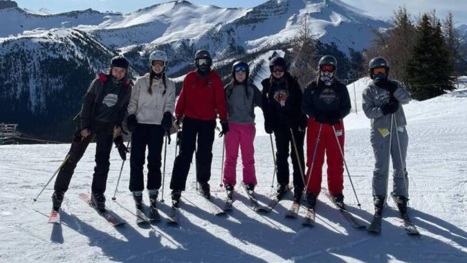 Schüler der Bawlf School stehen im Winter auf einem schneebedeckten Hang mit Bergen im Hintergrund.
