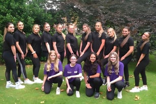 Eine Gruppe junger Frauen in schwarzen Outfits steht auf dem Campus des Baxter College im Grünen.