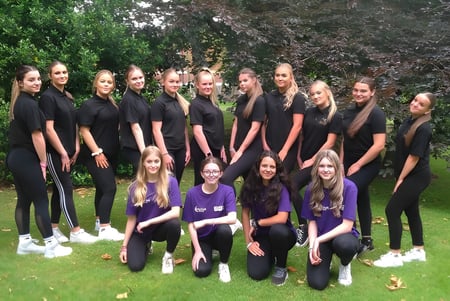Eine Gruppe junger Frauen in schwarzen Outfits steht auf dem Campus des Baxter College im Grünen.
