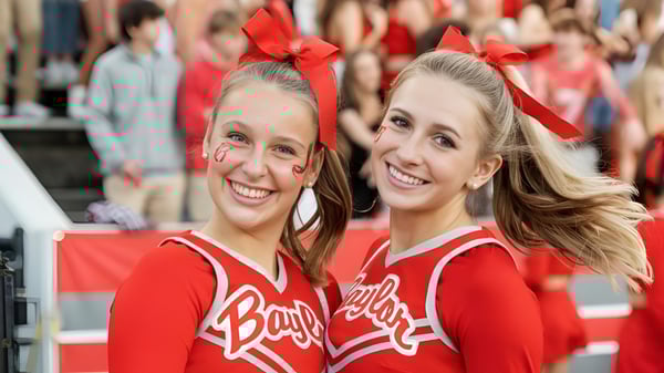Zwei lächelnde Cheerleader in roten Uniformen auf dem Campus der Baylor School vor einer Menschenmenge.