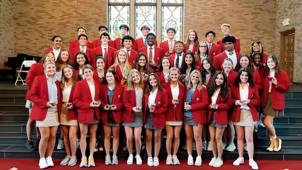 Eine Gruppe von Schülerinnen und Schülern der Baylor School steht in roten Roben auf der Treppe vor einem Gebäude mit Buntglasfenstern.
