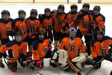 Eine Gruppe junger Hockeyspieler in orange-schwarzen Trikots auf der Eisbahn der Bayridge Secondary School.