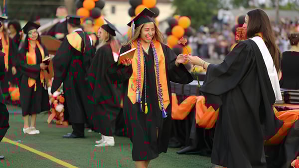 Eine Gruppe von Absolventinnen und Absolventen in schwarzen Talaren auf der Abschlussfeier der Bayridge Secondary School auf einer Wiese.
