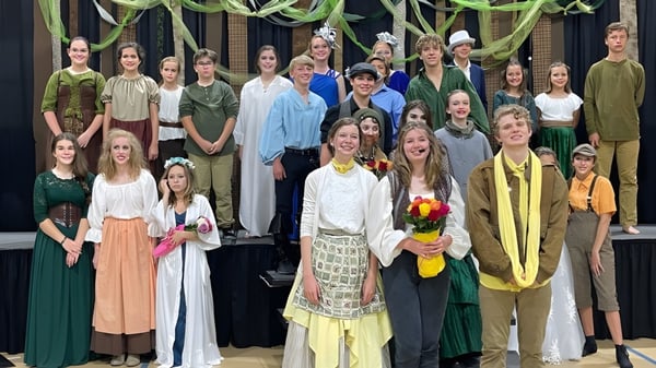 Eine Gruppe junger Schülerinnen der Bayshore Christian School steht auf einer Bühne vor dunklem Hintergrund mit Dekorationen.