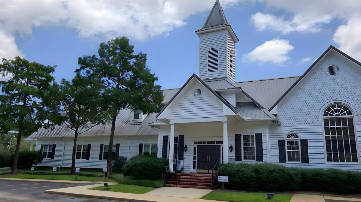 Eine weiße Holzkirche mit hohem Turm steht auf dem Gelände der Bayshore Christian School in einer grasbewachsenen Fläche.