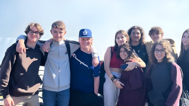 Eine Gruppe von Schülerinnen und Schülern steht zusammen im Freien auf dem Gelände der Bayside Secondary School vor klarem Himmel.