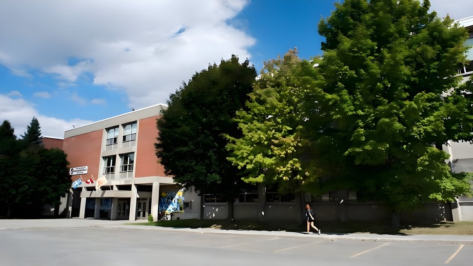 Das mehrstöckige Gebäude der Beaconsfield High School steht vor grünen Bäumen unter einem blauen Himmel mit Wolken.