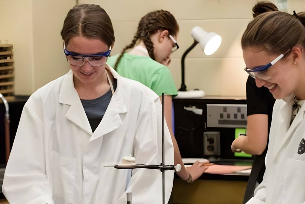 Drei Schüler der Beaconsfield High School führen im Labor eine wissenschaftliche Untersuchung mit Schutzbrillen und Laborkitteln durch.