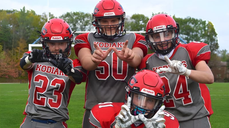 Vier Football-Spieler stehen auf dem Spielfeld der Bear Creek Secondary School vor Bäumen im Hintergrund.