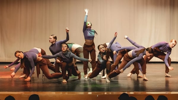 Eine Gruppe von Tänzern performt auf der Bühne der Bear Creek Secondary School mit erhobenen Armen vor einem hölzernen Hintergrund.