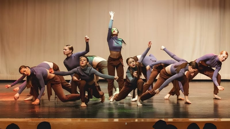 Eine Gruppe von Tänzern performt auf der Bühne der Bear Creek Secondary School mit erhobenen Armen vor einem hölzernen Hintergrund.
