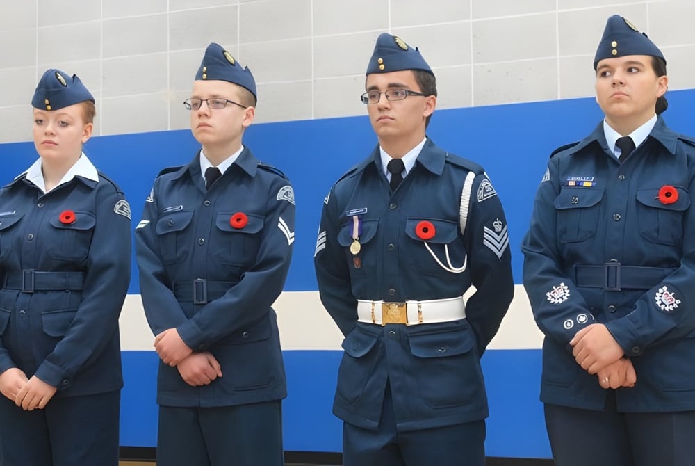 Vier Schüler der École Secondaire Beaumont Composite High School stehen in Militäruniformen vor blauem Hintergrund.