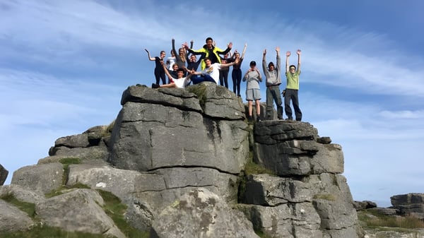 Eine Gruppe von Schülern steht auf einer felsigen Plattform unter klarem blauem Himmel auf dem Gelände der Bedales School.