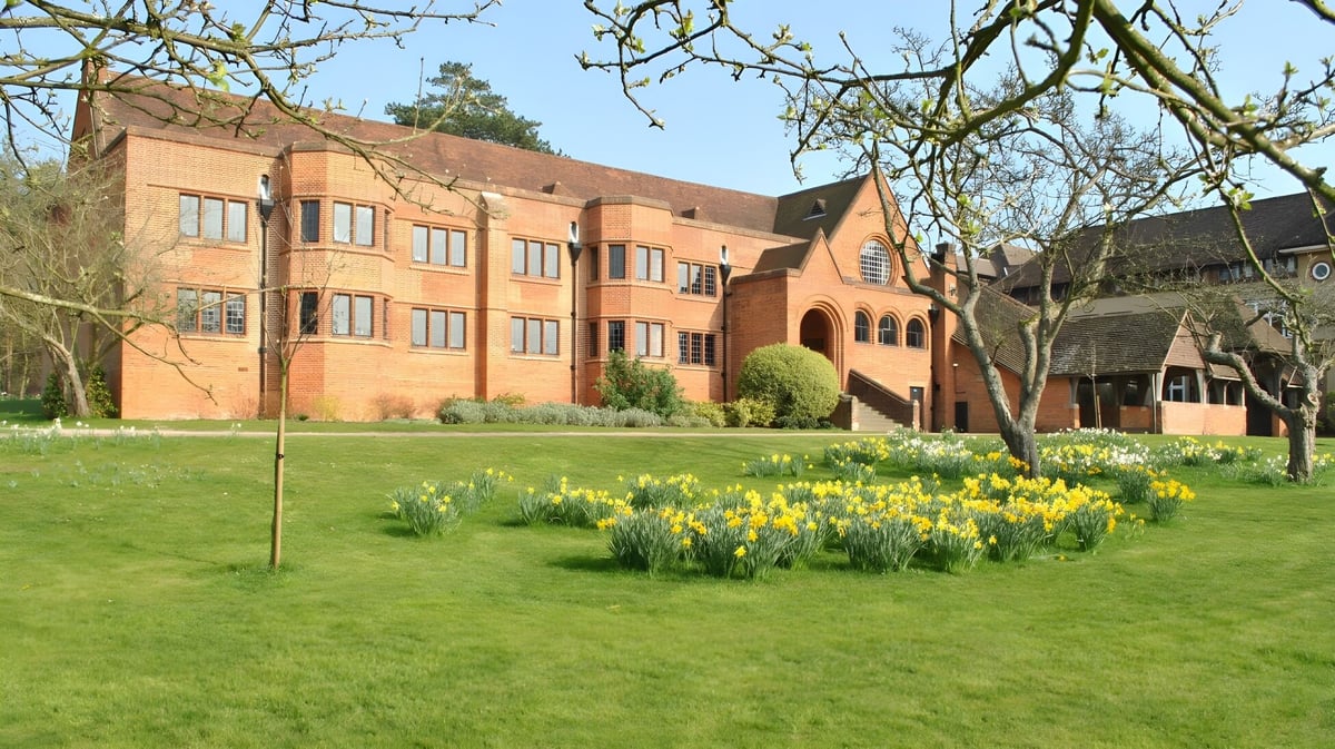 Das Backsteingebäude der Bedales School steht mehrstöckig im Hintergrund hinter einer grünen Wiese mit gelben Narzissen.