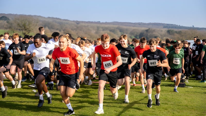 Eine große Gruppe von Läufern nimmt an einem Rennen auf einer Wiese vor dem Hintergrund von Hügeln und Bäumen auf dem Gelände der Bede's Senior School teil.