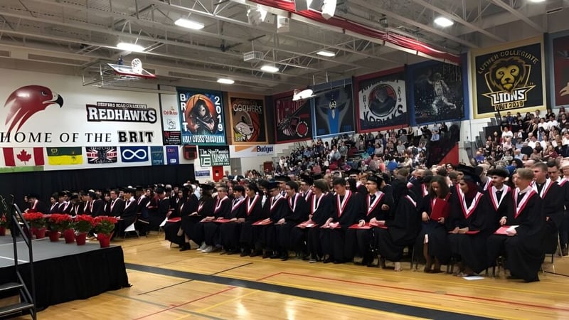 Schülerinnen und Schüler in Talaren stehen bei der Abschlussfeier des Bedford Road Collegiate in einer Sporthalle.