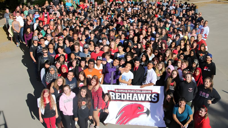 Viele Schülerinnen und Schüler halten auf dem Schulgelände von Bedford Road Collegiate ein Banner mit dem Maskottchen Redhawks.