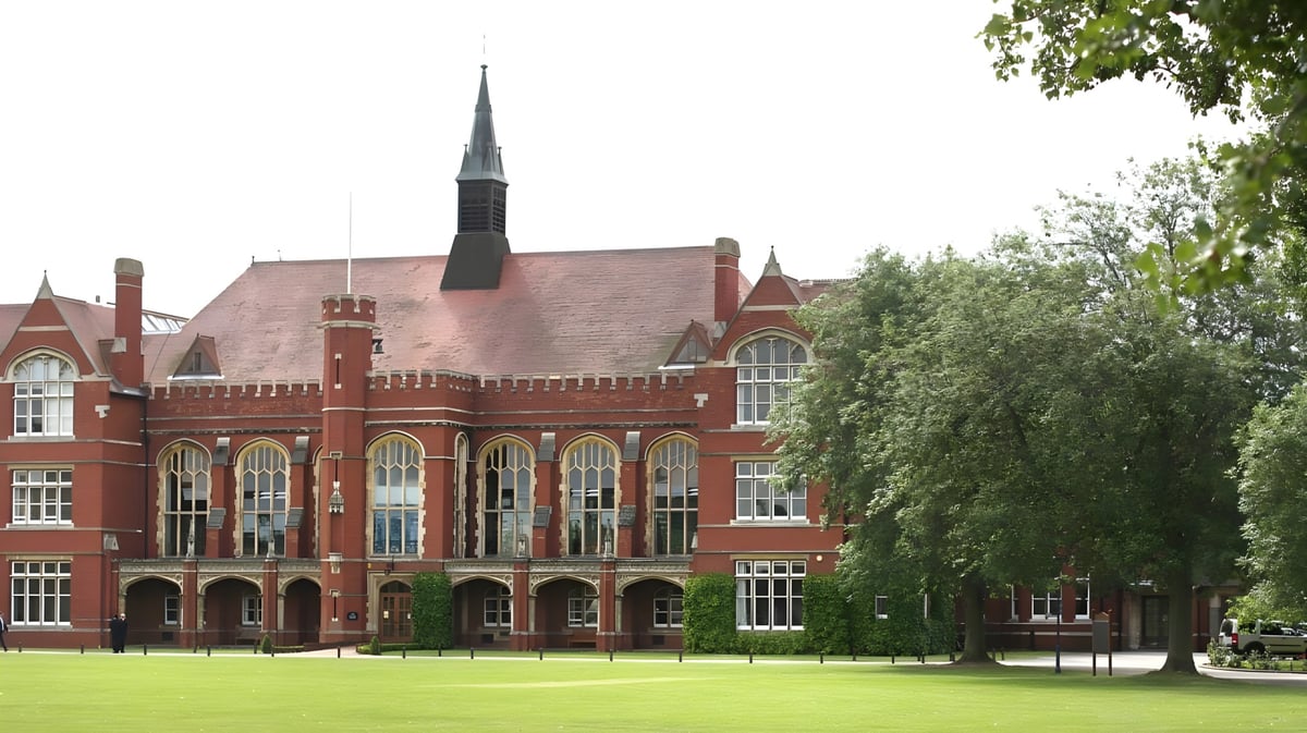 Das historische Backsteingebäude mit hohem Turm auf dem Campus der Bedford School ist von Bäumen umgeben.