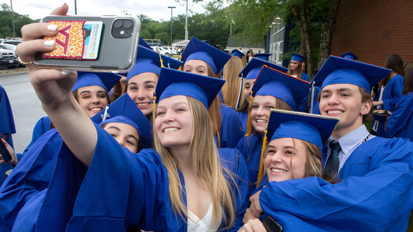 Eine Gruppe von Absolventen der Bedford School posiert in blauen Talaren für ein Selfie vor dem Campus.
