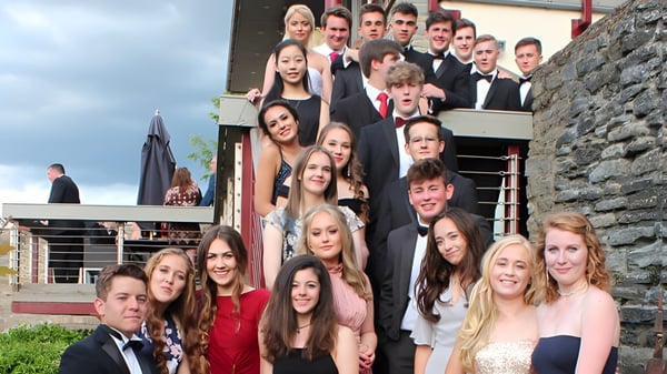 Eine Gruppe junger Erwachsener steht in formeller Kleidung vor einem Steingebäude auf dem Campus des Bedstone College.