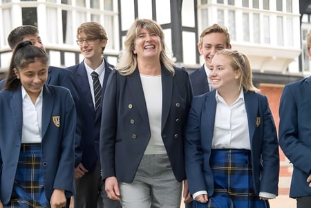 Eine Gruppe von Schülerinnen und Schülern steht fröhlich vor einem Gebäude mit großen Fenstern auf dem Campus der Bedstone School.