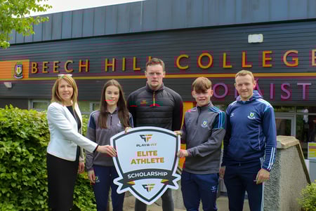 Schüler und Mitarbeiter stehen vor dem Gebäude des Beech Hill College und halten ein Schild mit der Aufschrift Elite Athlete Scholarship.