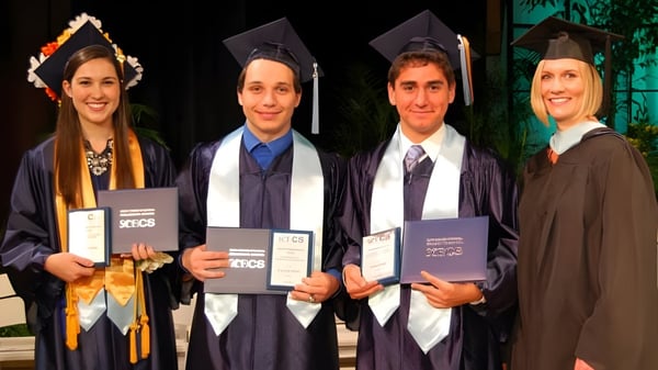 Vier Absolventen in Abschlussrobe auf dem Campus des Beech Hill College halten ihre Diplome im Freien.